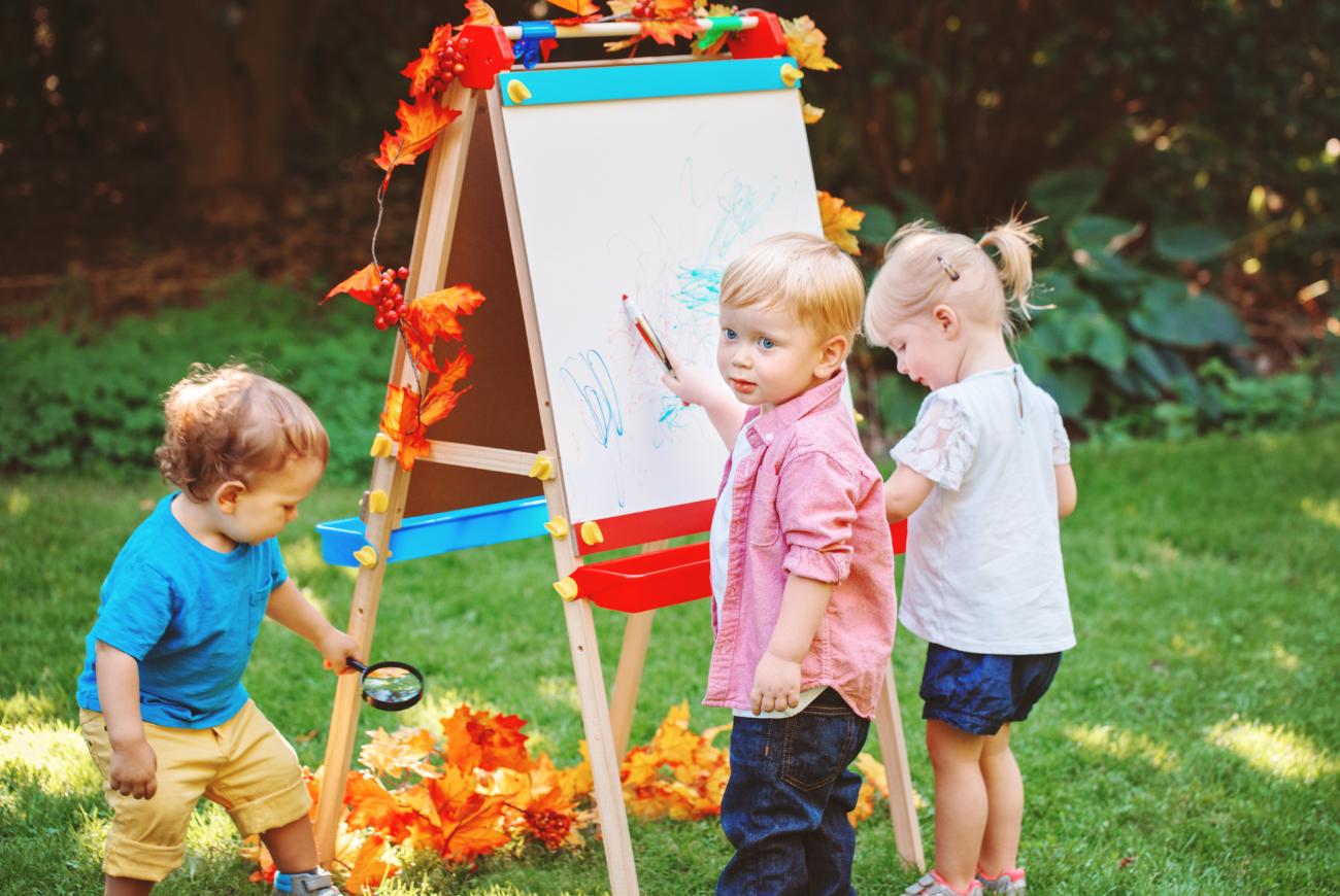 Three toddlers play with an easel together.