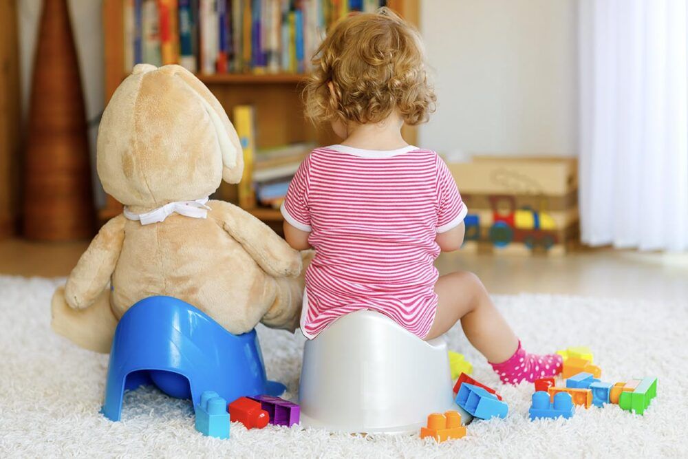 Baby potty training with teddy next to her.