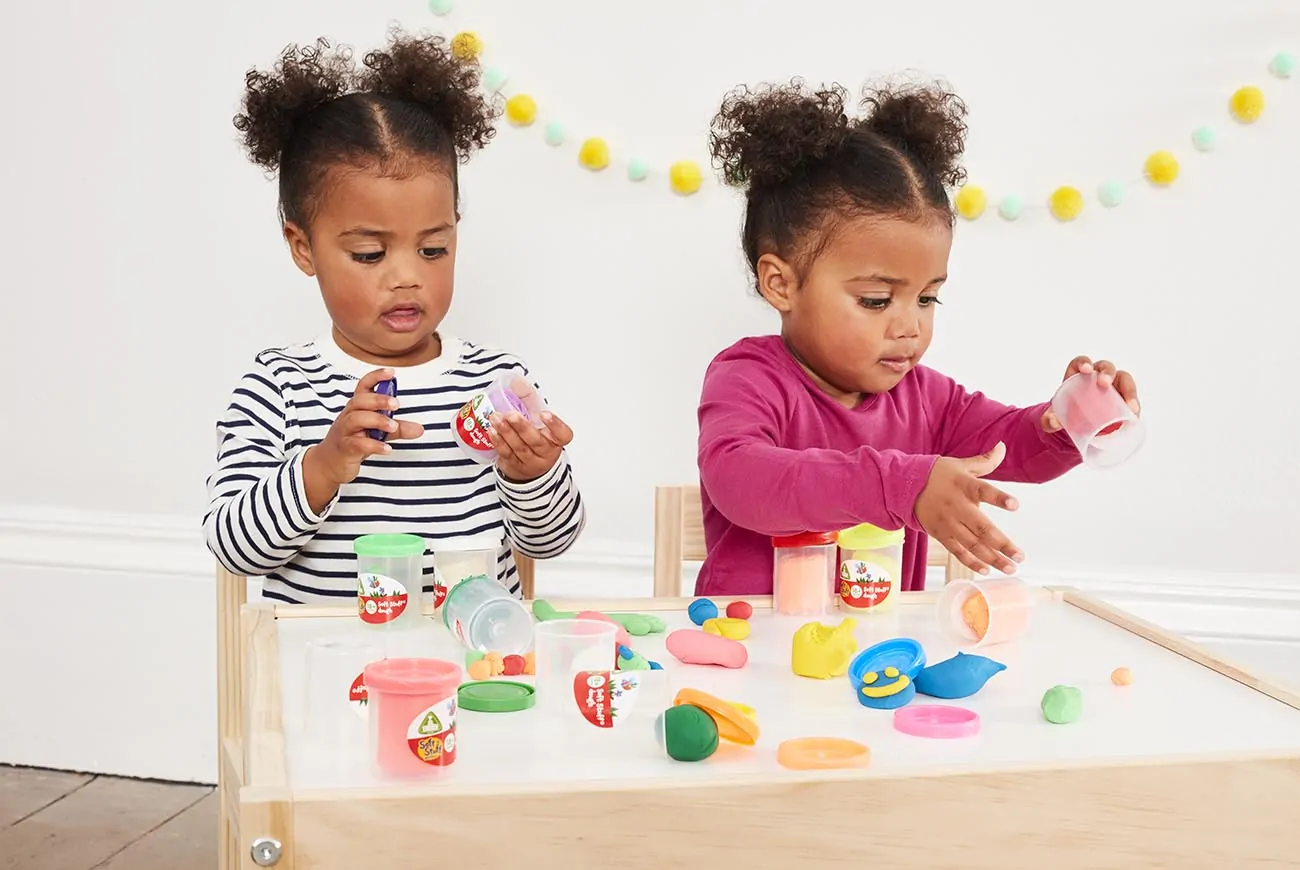 Two young sisters play with bright toys together on a table.