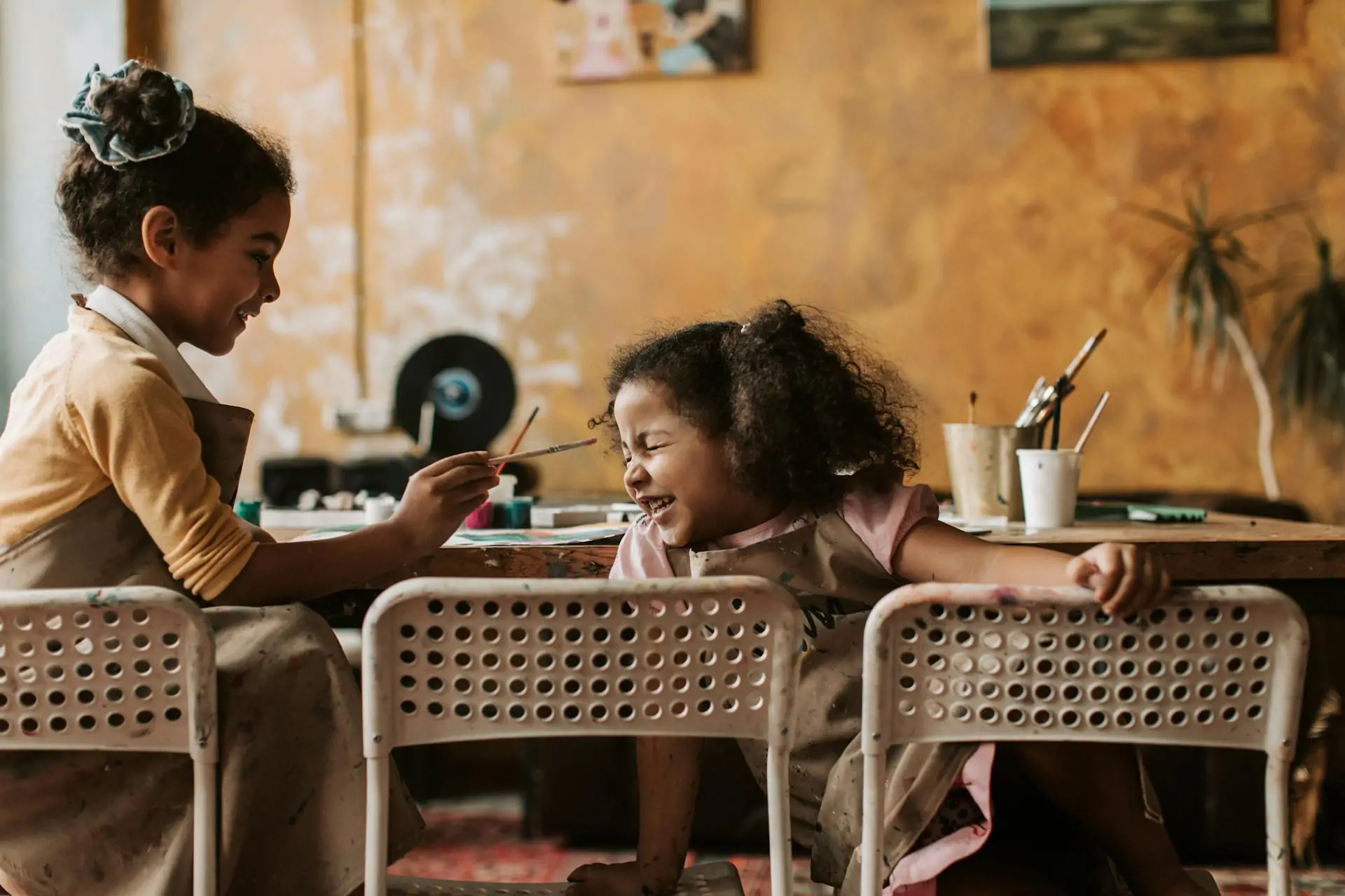 Two preschool children playing and laughing while sat at a table.