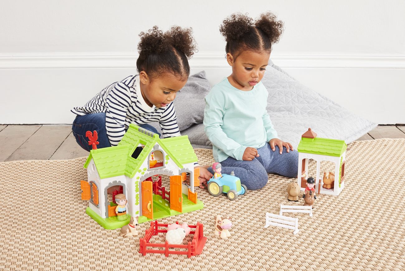 Two girls sat on the floor playing with a Happyland set.