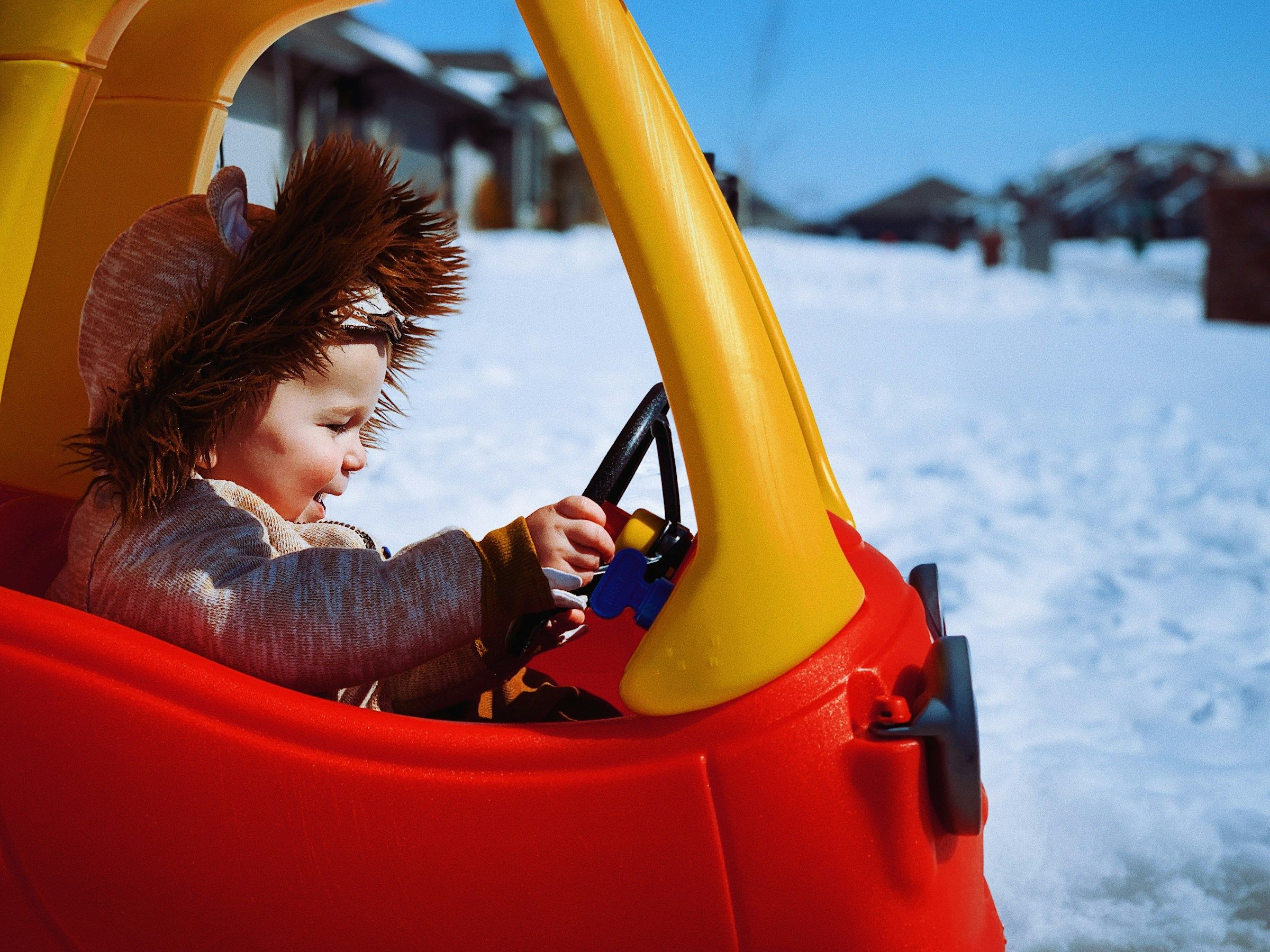 Child sits in a toy car steering the wheel.