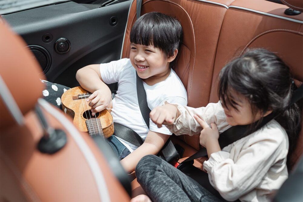 brother and sister in the back seat of a car with a ukelele on their laps