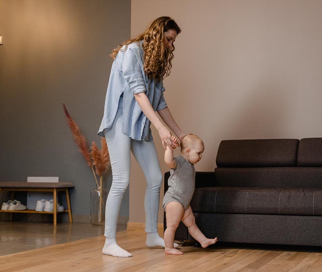 mum is holding baby's hands and helping baby to walk across the room