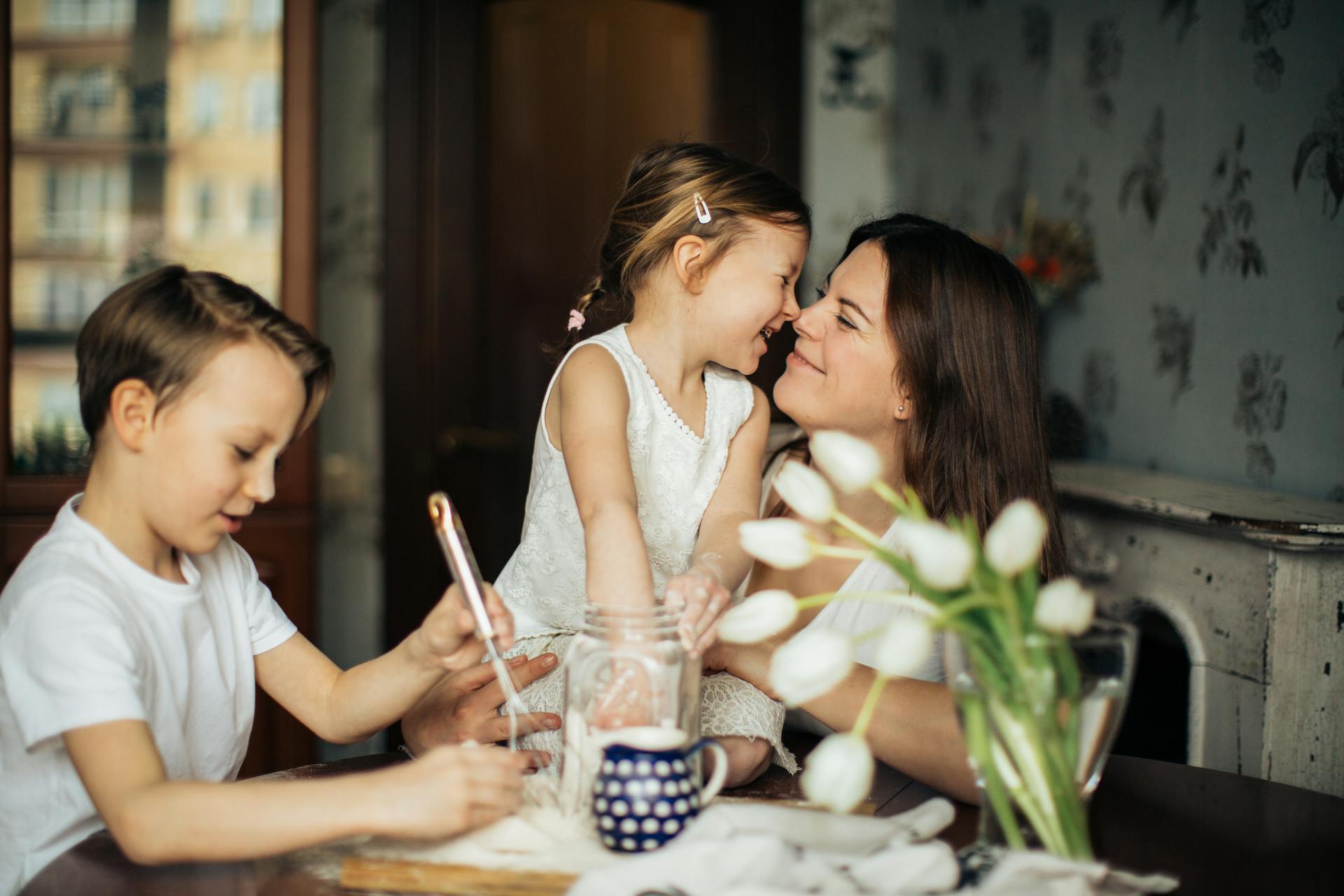 Sat around a table, a son plays with an object, and daughter cuddles up to mum.