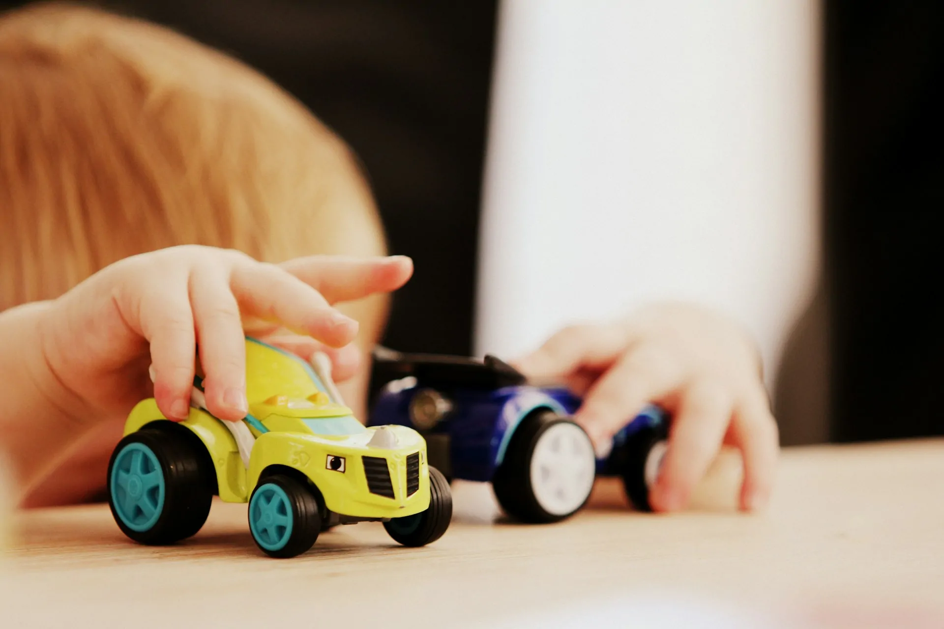 a child plays with two toy cars.