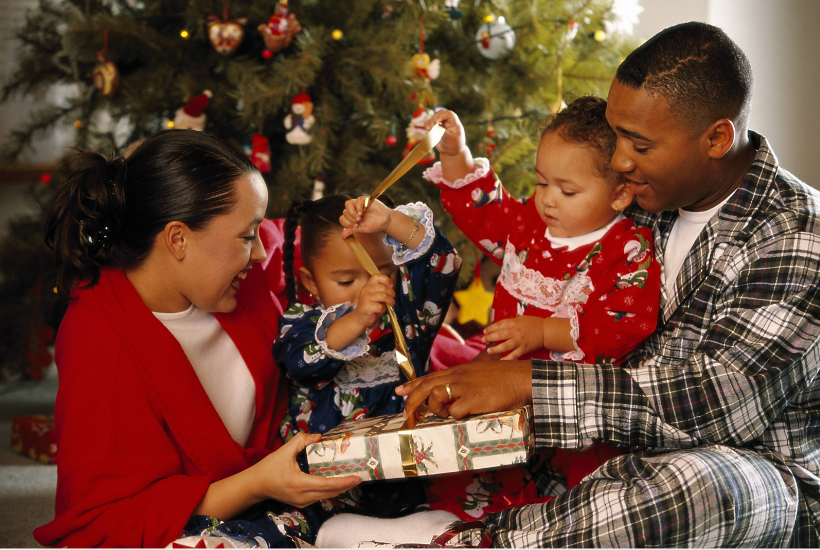 Family sat together opening up christmas presents.