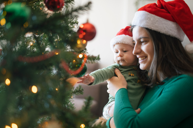 Mum abd baby by a christmas tree wearing christmas hats.