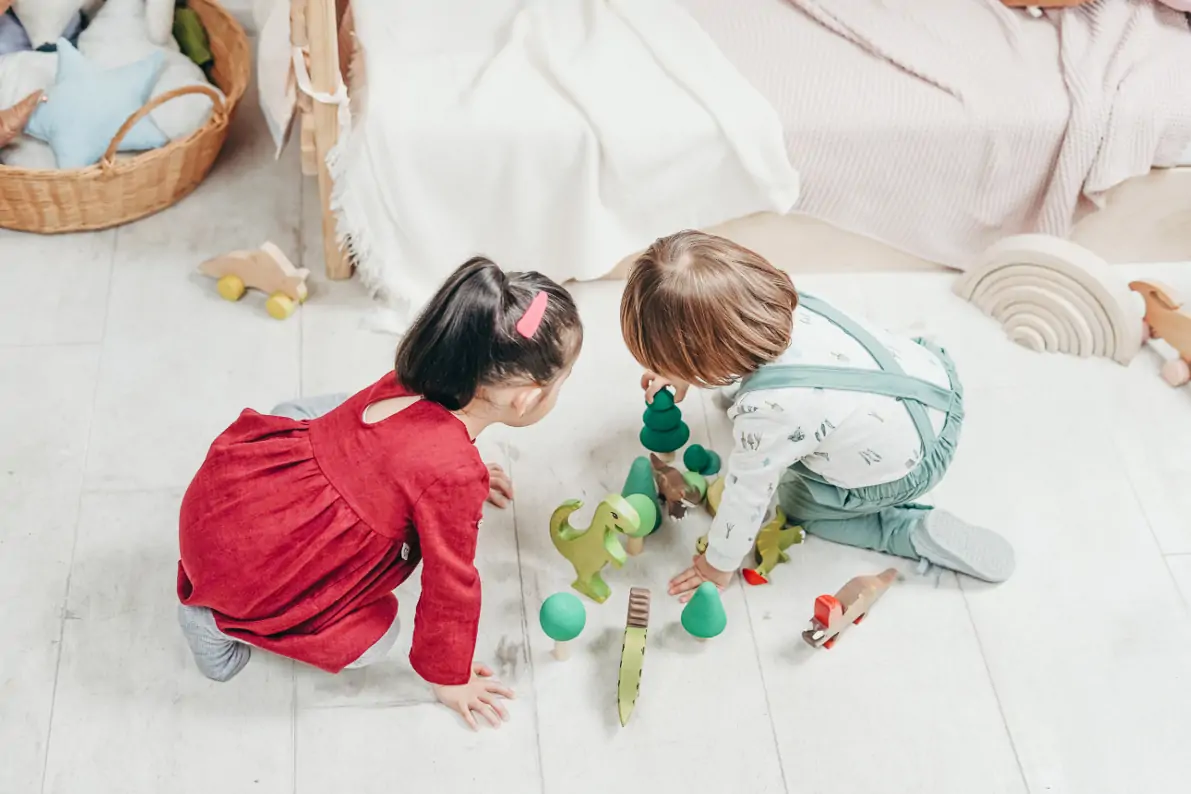 Two kids play on a bedroom floor with building blocks.