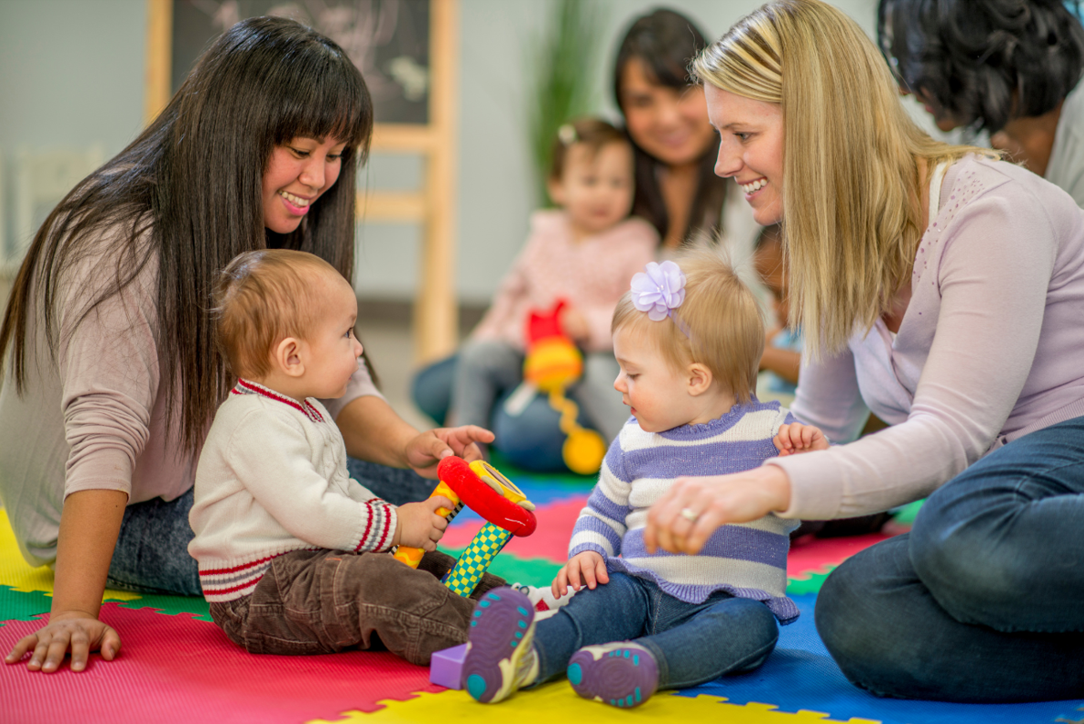 Two mums play with their children on the floor at an indoor play area.