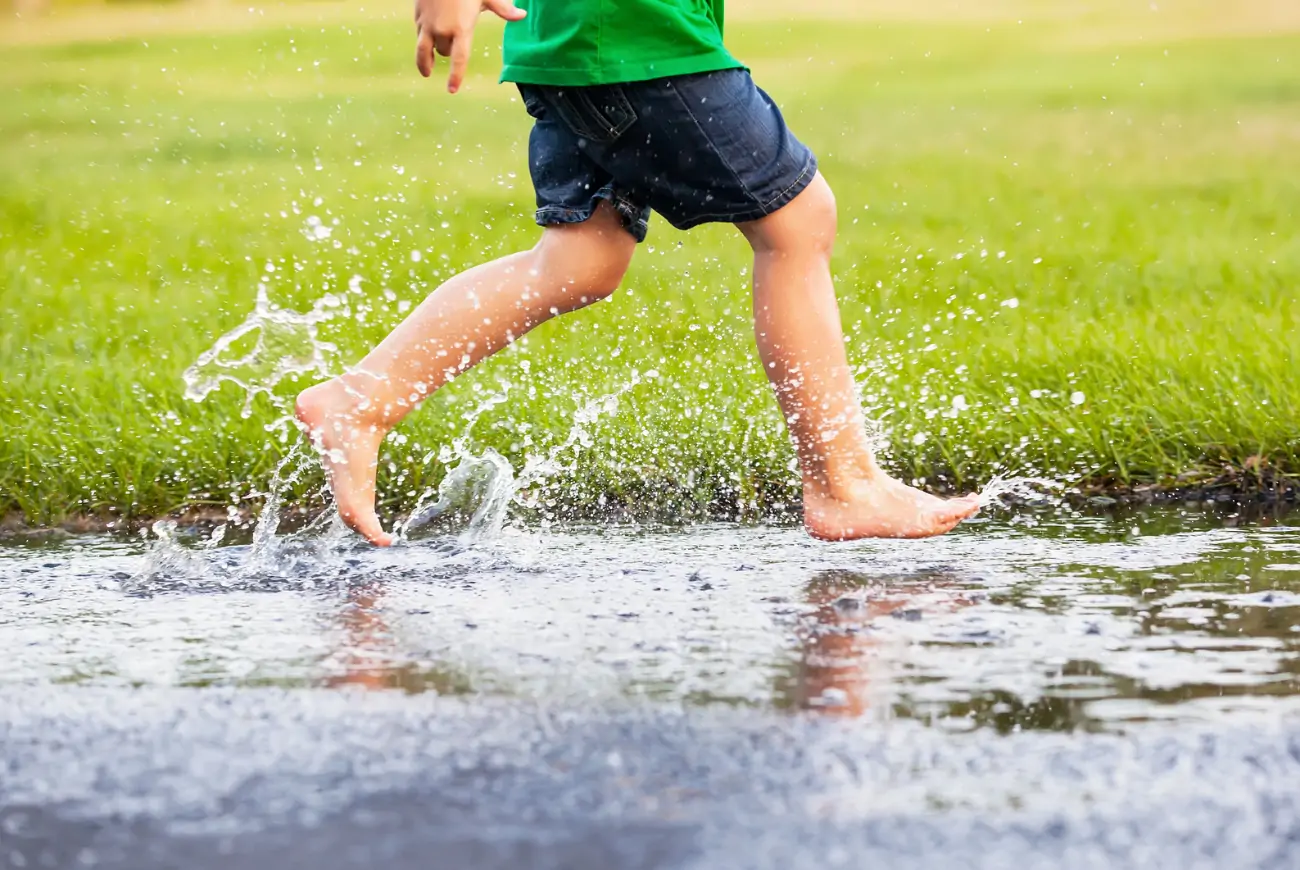 barefoot child runs through a puddle