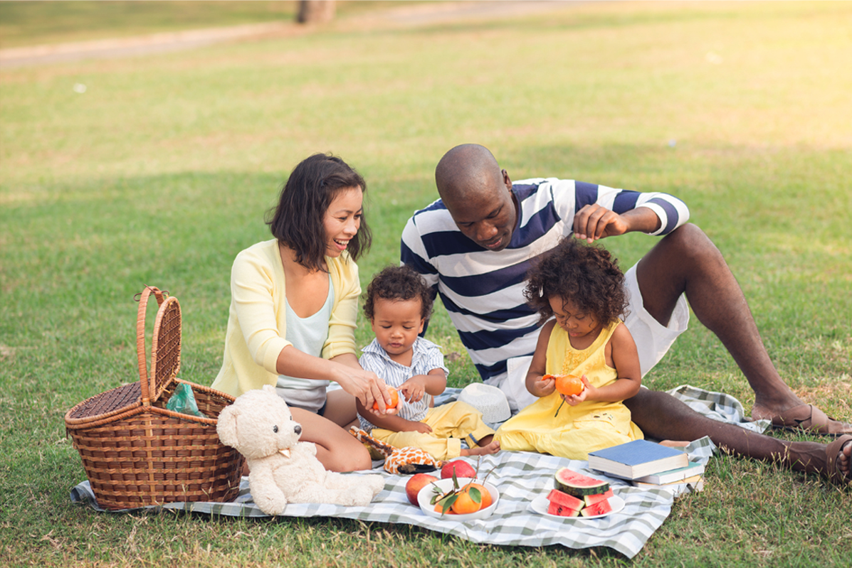 Family sat together in a park having a picnic.